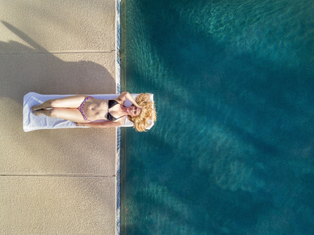 A blonde bikini model posing by a swimming pool