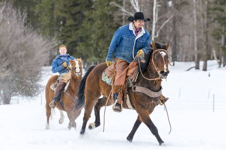 Cowboys round up a herd of horses as they're running through the snow in the mountainsの写真素材