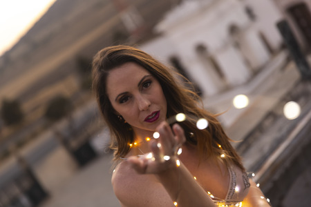 A gorgeous Hispanic Brunette model poses outdoors at sunset with small lights