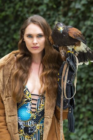 A gorgeous Hispanic Brunette model poses outdoors with a falcon outdoors at a hacienda