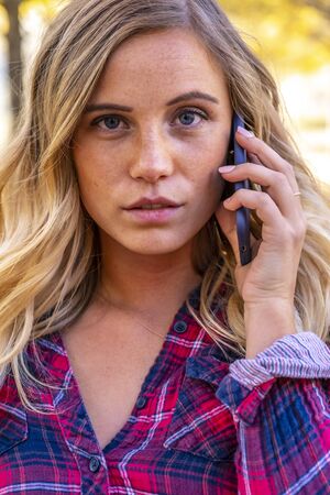 A gorgeous blonde model talks on her cellphone on an autumn day outdoors in a park