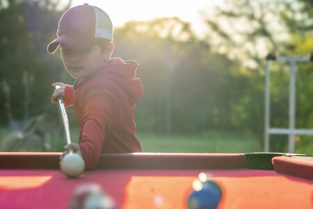 A small young boy plays pool in an outdoor environment