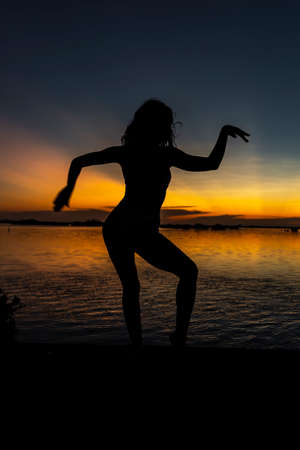 A beautiful blonde model poses sexy silhouetted as she poses with the rising sun behind her on a exotic Caribbean beachの写真素材