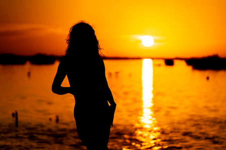 A beautiful sexy latin model is silhouetted as she poses with the rising sun behind her on a exotic Caribbean beachの写真素材