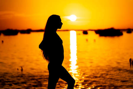 A beautiful sexy latin model is silhouetted as she poses with the rising sun behind her on a exotic Caribbean beachの写真素材