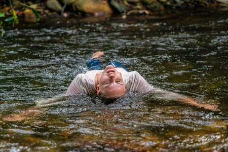 A gorgeous blonde model plays around in a river in the woods on a summers dayの写真素材
