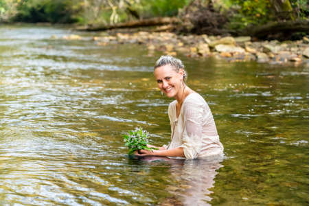 A gorgeous blonde model plays around in a river in the woods on a summers day