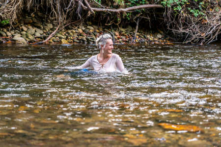 A gorgeous blonde model plays around in a river in the woods on a summers dayの写真素材