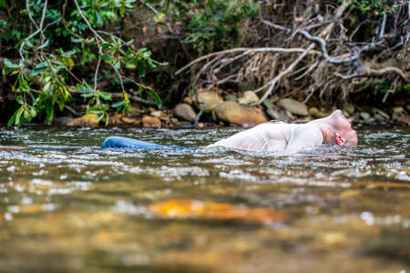 A gorgeous blonde model plays around in a river in the woods on a summers day
