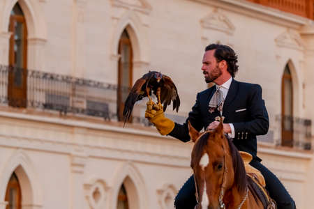 A handsome Mexican Charro poses in front of a hacienda in the Mexican countryside while holding a...