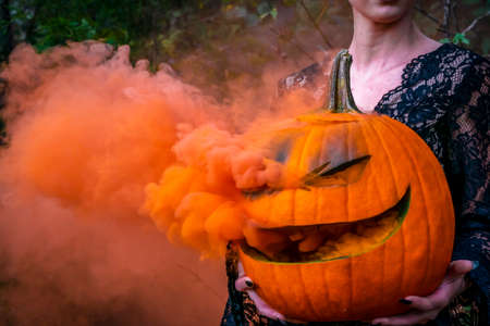A beautiful blonde model wearing all black poses with a smoking pumpkin in an outdoor environmentの写真素材