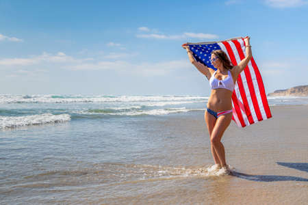 A gorgeous brunette model poses with an American Flag At The Beachの写真素材