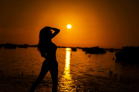 A beautiful nude latin model is silhouetted as she poses with the rising sun behind her on a exotic...