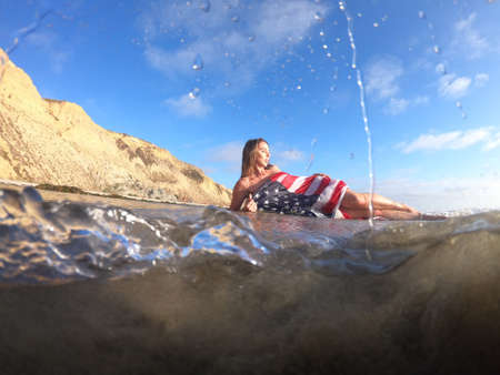 A gorgeous brunette model poses nude with an American Flag At The Beach
