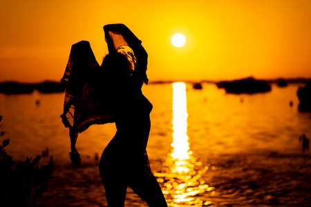 A beautiful nude latin model is silhouetted as she poses with the rising sun behind her on a exotic Caribbean beachの写真素材