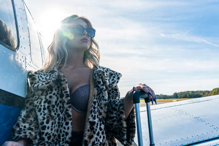 A gorgeous young blonde model poses outdoors with a single engine aircraft at a local airport