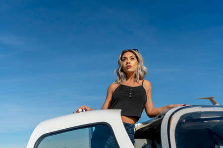 A gorgeous young blonde model poses outdoors with a single engine aircraft at a local airport