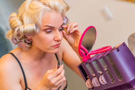 A gorgeous blonde model does her makeup before posing in lingerie in a home environment