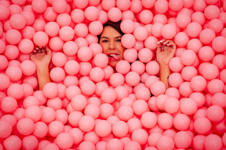 A beautiful asian model plays in a colorful room with a huge amount of plastic balls