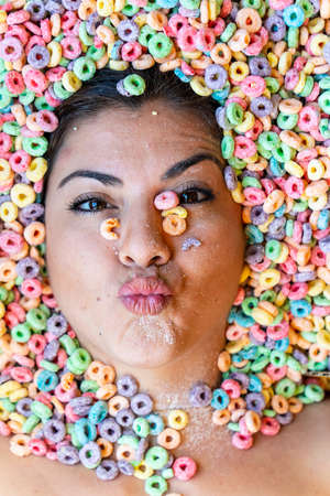 A gorgeous young hispanic model is covered in breakfast cereal only showing her face