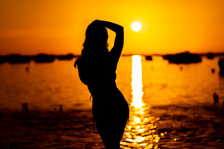 A beautiful latin model is silhouetted as she poses with the rising sun behind her on a exotic Caribbean beachの写真素材