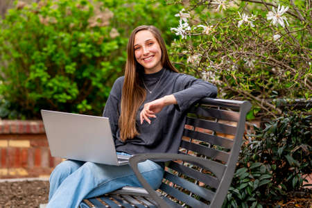 A gorgeous brunette model works on her computer outdoors while enjoying the spring weatherの写真素材