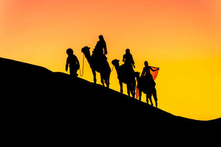 Three passengers and their handler travel in the Saharan Desert in Moroccoの写真素材