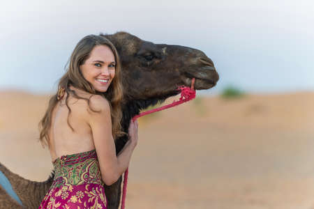 A beautiful model rides a camel through the Saharan Desert in Moroccoの写真素材