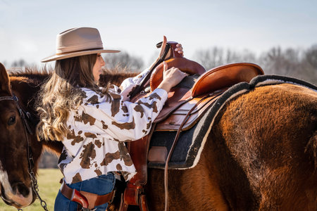 A beautiful brunette cowgirl poses with her horse before riding in the countryの写真素材