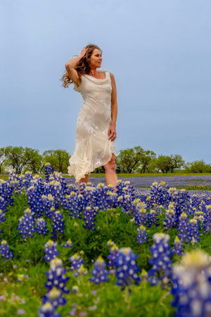 A beautiful brunette model enjoys a field of Bluebonnet flowers on a spring dayの写真素材