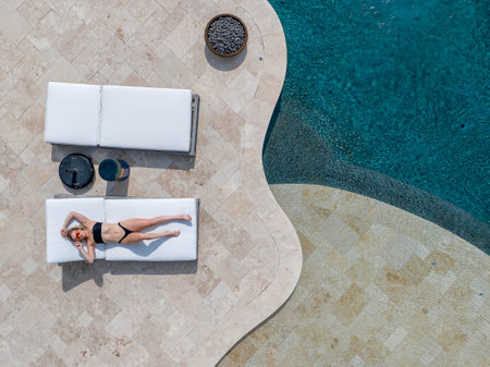 A gorgeous blonde bikini model enjoys a day off at home lounging by the swimming pool