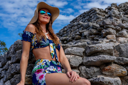 A radiant young woman explores the Xcambo Mayan ruins, her presence weaving elegance with ancient history, under the Caribbean sun's golden embraceの写真素材