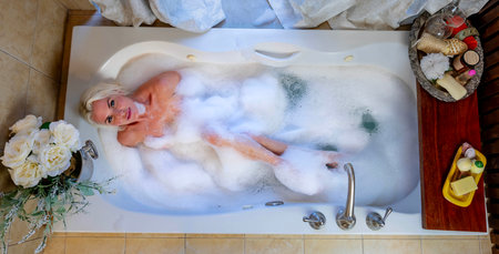 Blonde allure unfolds as a nude model luxuriates in a round home bathtub, embodying elegance and relaxation in a captivating and serene bathing momentの写真素材