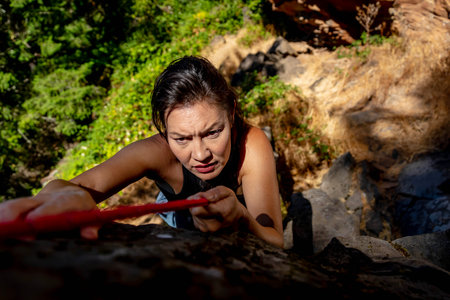 A stunning mixed-race brunette fitness model ascends a rugged mountain trail in the Pacific Northwest, her toned physique glowing in the early afternoon sunlight, surrounded by lush greenery and towering peaks.の写真素材