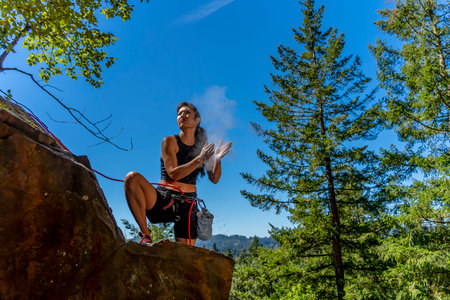 A stunning mixed-race brunette fitness model ascends a rugged mountain trail in the Pacific Northwest, her toned physique glowing in the early afternoon sunlight, surrounded by lush greenery and towering peaks.の写真素材