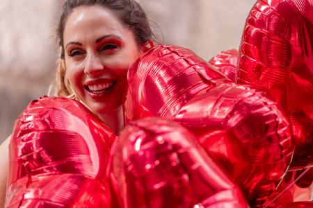 A beautiful brunette strolls down a bustling city street, clutching a dozen red heart-shaped balloons. Her smile reflects excitement as she heads to a special Valentineâs Day getaway to meet her lover.の写真素材