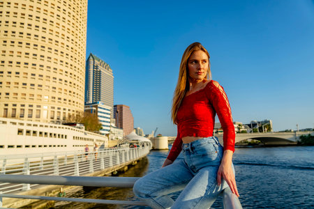 A stunning young blonde model strikes a pose downtown, her chic summer outfit perfectly contrasting against the vibrant blue sky. She exudes confidence, radiating warmth and effortless style.の写真素材