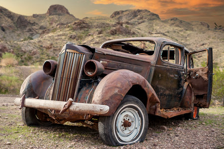 An old rusted vehicle sits abandoned in the arid Nevada desert, its weathered frame blending with the dry, cracked earth and sparse vegetation, epitomizing the stark, desolate beauty of the landscape.の写真素材