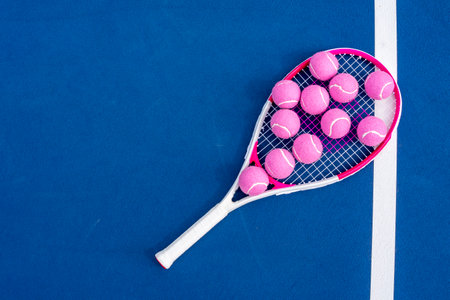 Bright pink tennis balls rest scattered on the vibrant blue court, their fuzzy surfaces glowing...