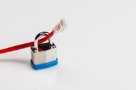 An Ethernet cable coiled with a metal padlock around its connector lies on a white background, symbolizing cyber security, data protection, and the safeguarding of digital networks.の写真素材