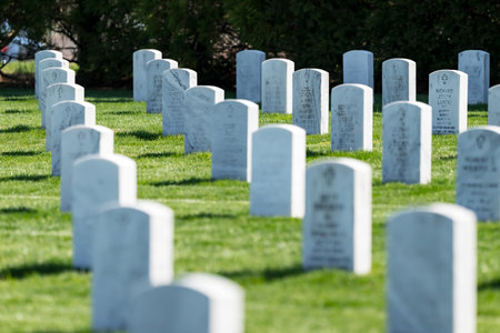 Symmetrical rows of gravestones adorned with American flags honor fallen heroes at a veterans cemetery. Lush green grass and manicured lawns set a serene scene for Memorial Day remembrance.の写真素材