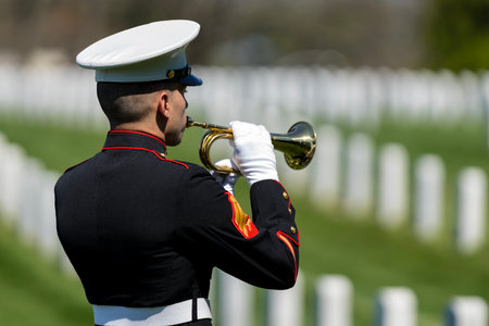 A poignant moment unfolds as a Marine plays taps, honoring a fallen veteran with a solemn salute, marking their internment at a national military cemetery.のeditorial素材