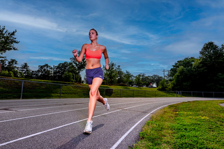 An athletic teen trains hard on a sunlit track, pushing through intense drills on a hot summer...