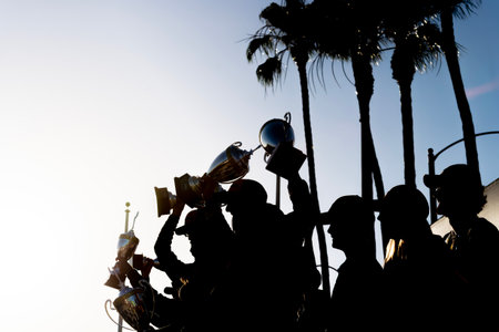 Silhouettes of race winners stand triumphantly in victory lane, trophies raised high as confetti...