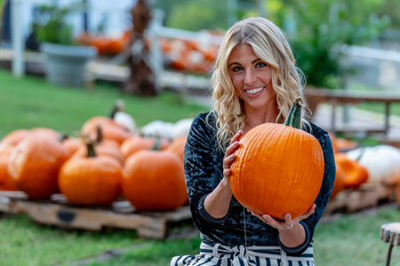 A stunning blonde model poses in a vibrant pumpkin field, wearing a stylish autumn outfit with a...