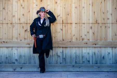 A gorgeous blonde model in cowgirl gear poses with a revolver in the American Southwest, framed by...