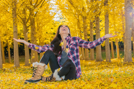 A beautiful young woman poses gracefully against golden fall leaves, her smile radiant as she...