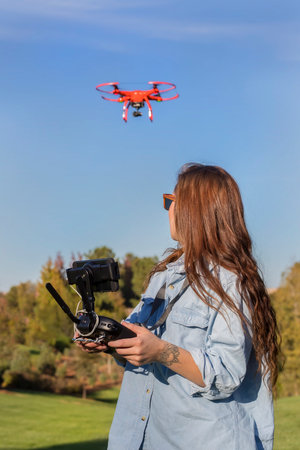 A beautiful young woman skillfully pilots a drone under the bright sun, practicing maneuvers with...