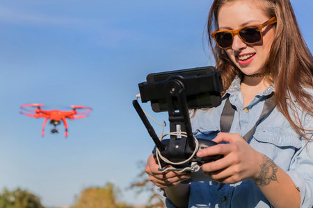 A beautiful young woman skillfully pilots a drone under the bright sun, practicing maneuvers with...