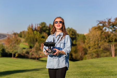 A beautiful young woman skillfully pilots a drone under the bright sun, practicing maneuvers with...